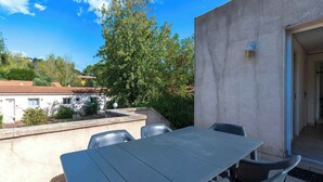 An outdoor patio with a table and chairs, a concrete wall, and a door leading to an interior space.