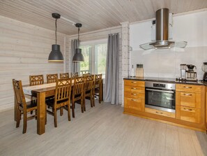 A wooden dining table with chairs, a kitchen with wooden cabinets, a stove, and pendant lights. - Villa valo by Interhome (Lieksa)