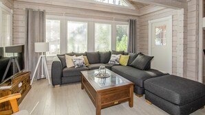 A spacious living room with a large sectional sofa, a wooden coffee table, and a TV on a wooden stand.