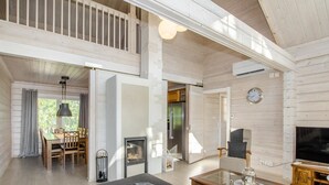A spacious living area with a high ceiling, a dining area with a table and chairs, a fireplace, and a television.