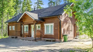 A wooden cabin with a porch, a chimney, and a gravel driveway.