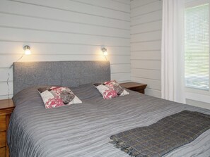 Ett sovrum med en säng, två sängbord, en lampa och ett fönster med persienner.