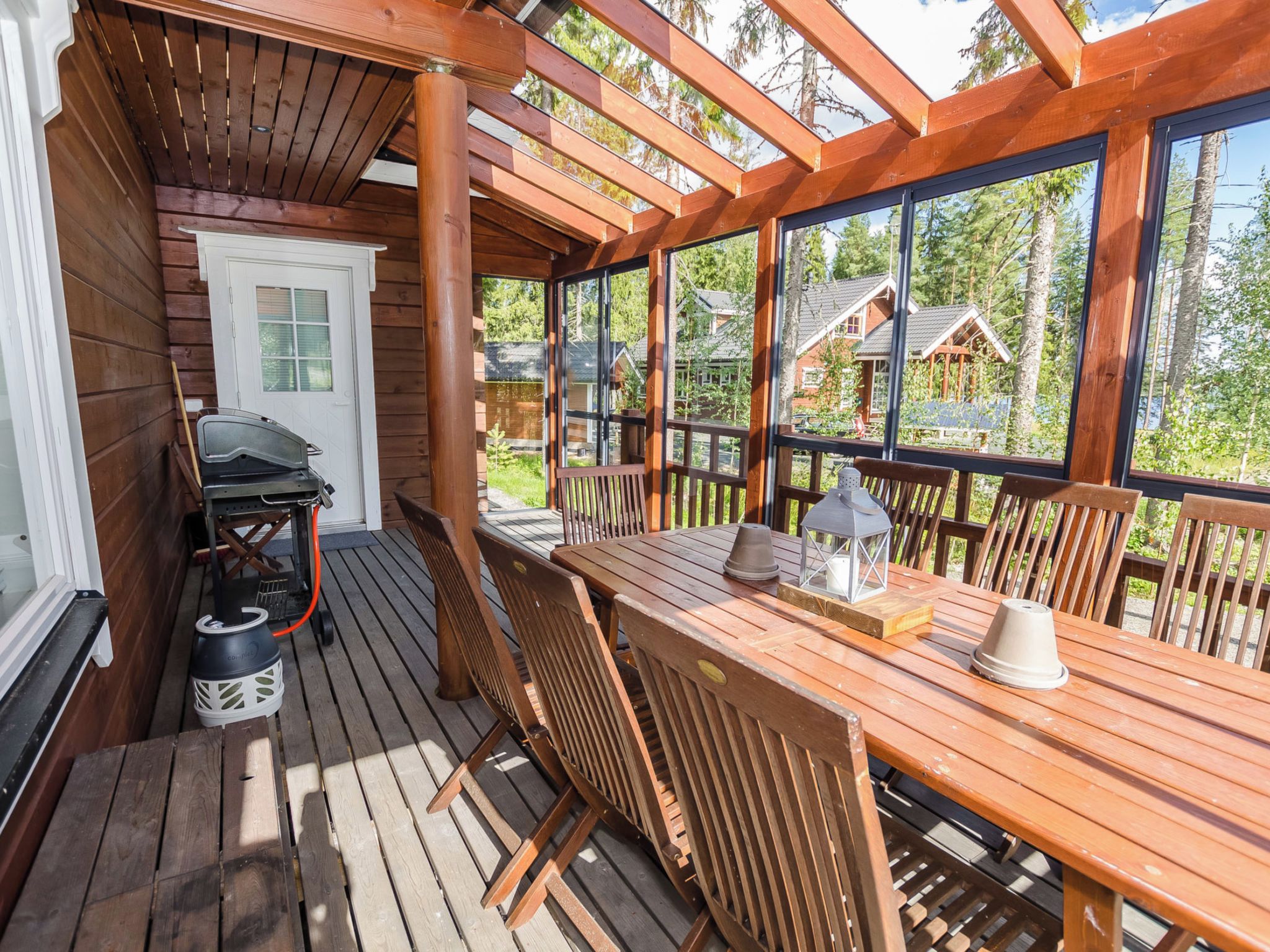 Eine Holzterrasse mit Tisch, Stühlen, einem Grill und einer Laterne.