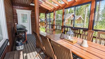 Eine Holzterrasse mit Tisch, Stühlen, einem Grill und einer Laterne.