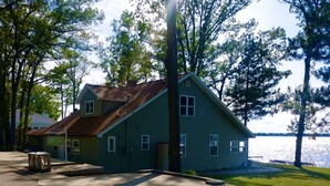 A two-story house with a sloped roof, a front porch, and a view of a lake. - New Listing! Lake front cottage with 100' of private sandy beach (Prudenville)