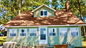 A single-story house with a green exterior, a chimney, and a front porch with outdoor furniture. - New Listing! Lake front cottage with 100' of private sandy beach (Prudenville)