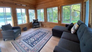 A cabin interior with a large window overlooking a lake, a patterned rug, and a sofa.