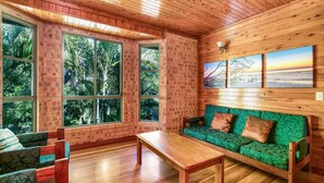 Una habitación acogedora con un banco de madera, un sofá verde con cojines estampados y ventanas amplias que dan a un follaje exuberante.