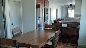 A spacious kitchen with wooden cabinets, a stainless steel refrigerator, and a dining area with a wooden table and chairs. - Get away from the hustle and bustle in an outdoor paradise! (Saratoga)