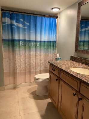 Bathroom features a shower curtain with a beach scene, a toilet, sink, and cabinets.