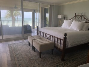 Relax in this serene bedroom with a large bed, plush ottoman, and sliding glass door leading to a balcony with ocean views.