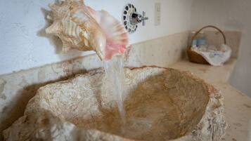 Un lavabo de piedra con agua saliendo de un grifo, una concha decorativa y una cesta al fondo.