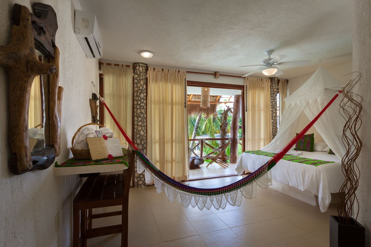 A room with a hammock, a bed with a canopy, a wooden bench, and a view of the outdoors.