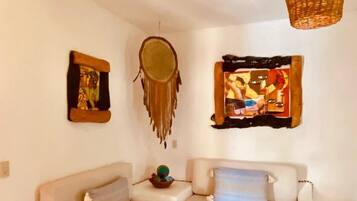 A living room with a white sofa, a glass coffee table, and wall art including a dreamcatcher and a framed picture.