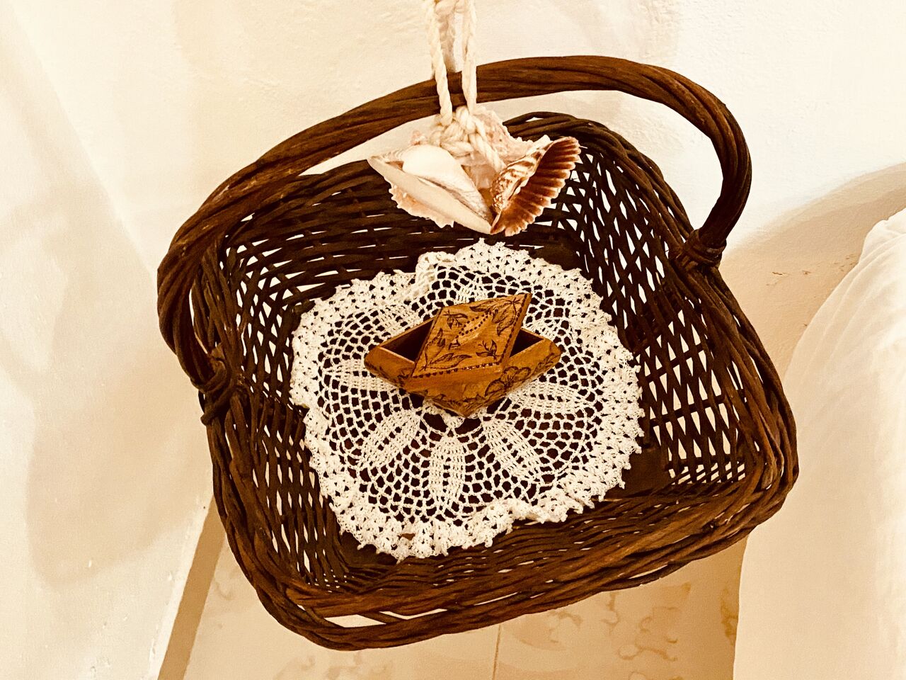 Uma cesta de vime com um jogoalho branco de crochê e uma caixa decorativa.