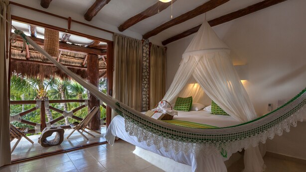 Een hangmatbed met een hemelbed, een houten terras en uitzicht op palmbomen.