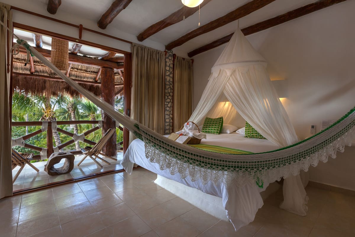A hammock bed with a canopy, a wooden deck, and a view of palm trees.