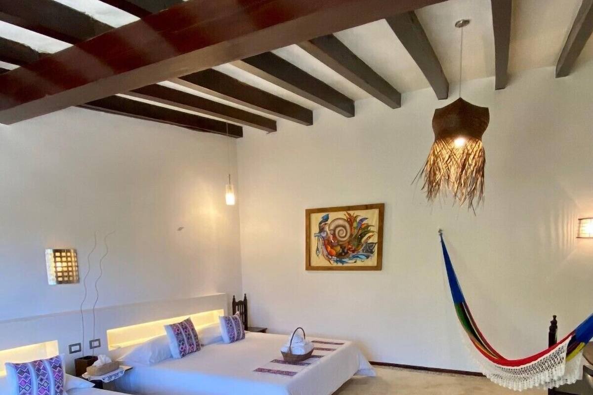 A hotel room with two beds, a hammock, a painting, and a ceiling light fixture.