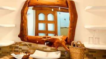 Un baño con un espejo de marco de madera, un lavamanos blanco, una cesta de mimbre y un pequeño estante con cristalería.