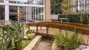 Un pont en bois enjambant un élément aquatique dans un espace extérieur aménagé, avec un bâtiment en arrière-plan.