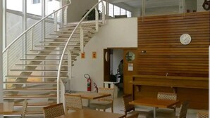 Un vaste espace intérieur doté d’un escalier central, de nombreuses tables et chaises, et de grandes fenêtres laissant entrer la lumière naturelle.