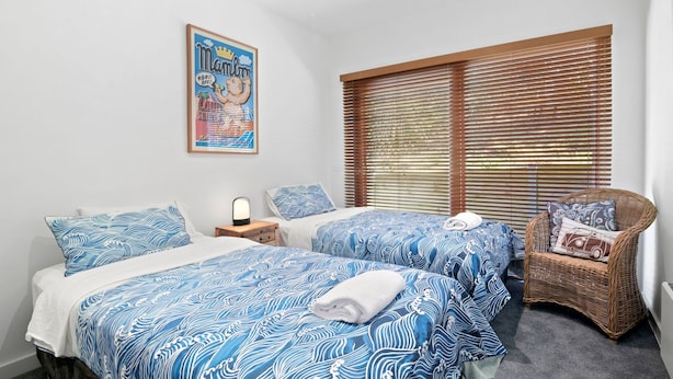 A bedroom with two beds, a poster on the wall, and a window with blinds.