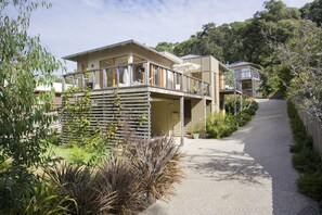 A residential building with a balcony, a pathway leading to it, and surrounding vegetation.