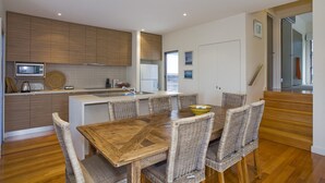 A modern kitchen with wooden cabinets, a built-in oven, and a dining area with a wooden table and wicker chairs.