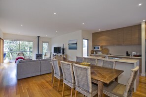 A modern kitchen with a dining area, wooden flooring, and a large window.