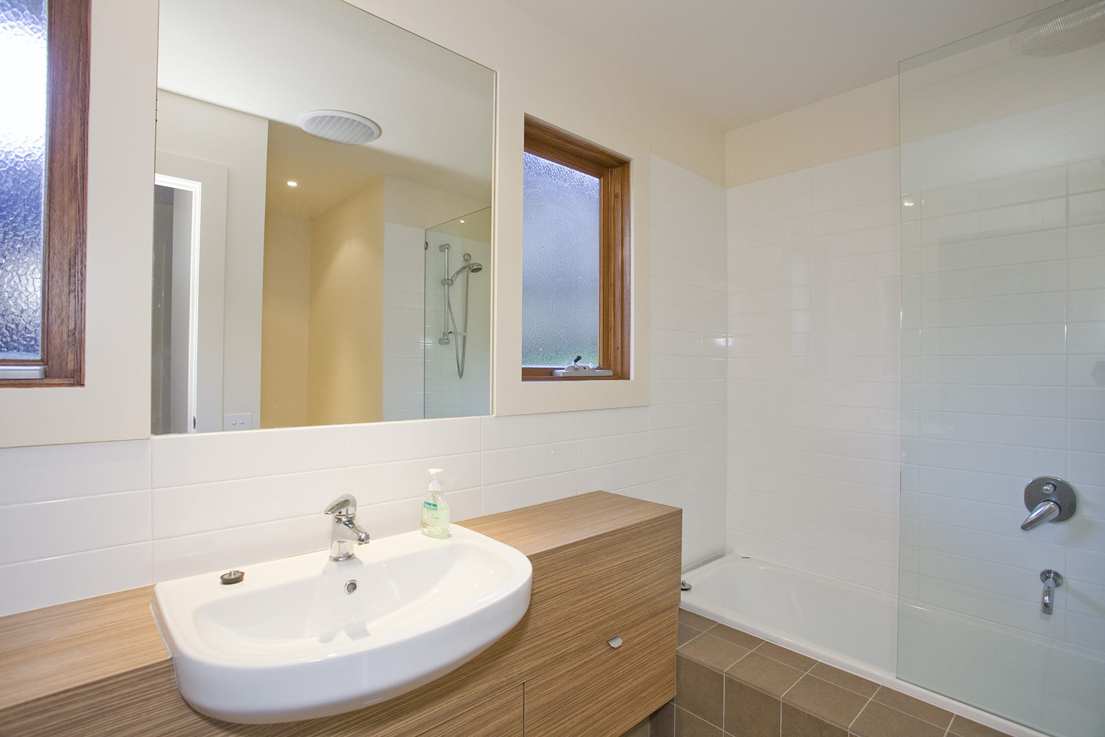 A bathroom with a white sink, a mirror, a window, and a shower.