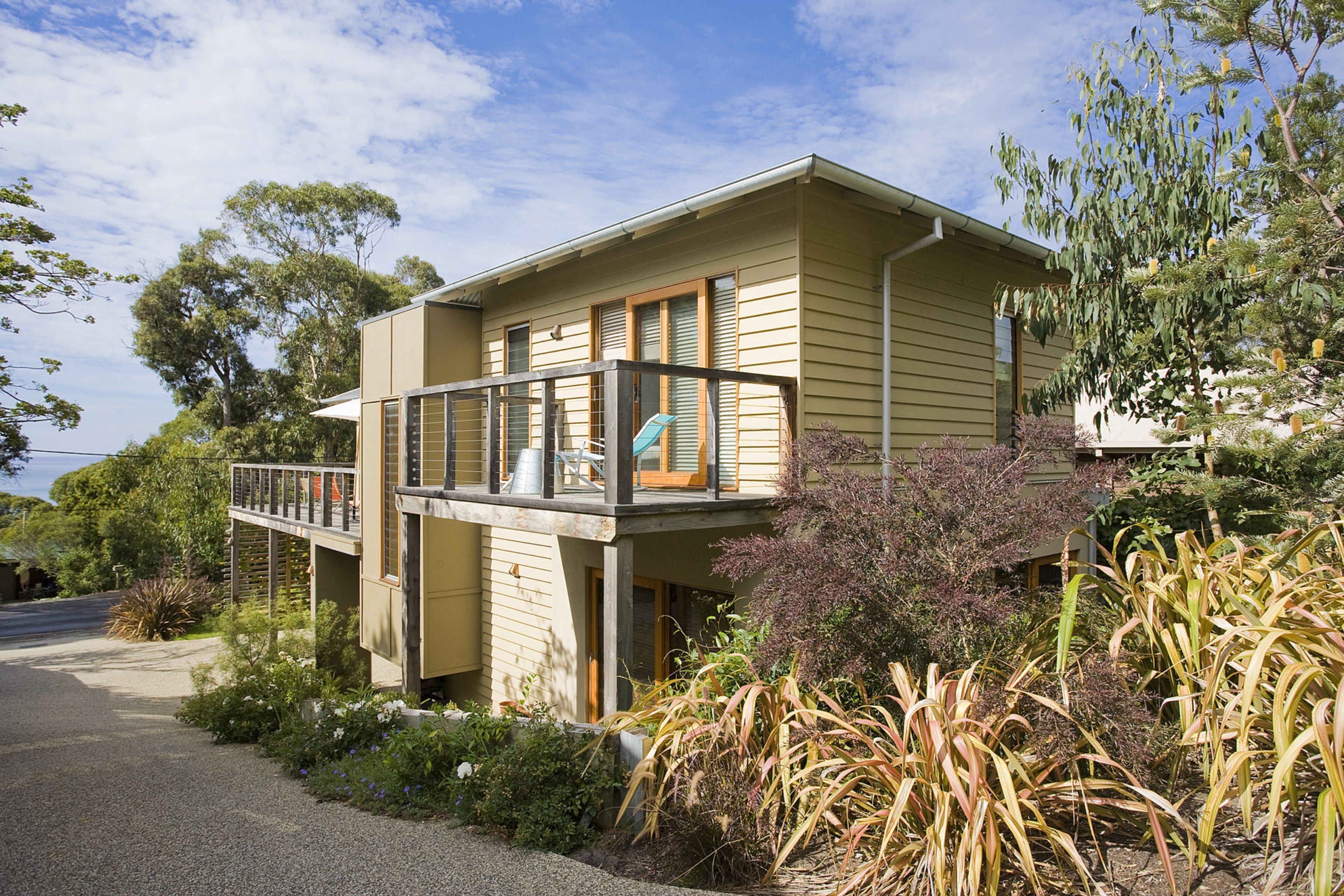 A two-story house with a balcony, surrounded by vegetation and trees.