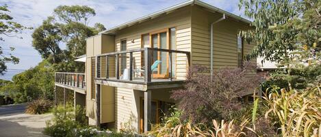 A two-story house with a balcony, surrounded by vegetation and trees.