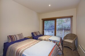 A bedroom with two beds, a wicker chair, and a large window with blinds.