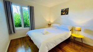 Een slaapkamer met een groot bed, twee bedlampen, een raam met gordijnen en een schilderij aan de muur.