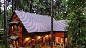 A log cabin with a metal roof, stone foundation, and a gravel driveway. - Bears 'n Biscuits Cabin, Sleeps 14, Hot tub, Playset, Pool Tbl, 4 brms, 3 baths (Broken Bow)