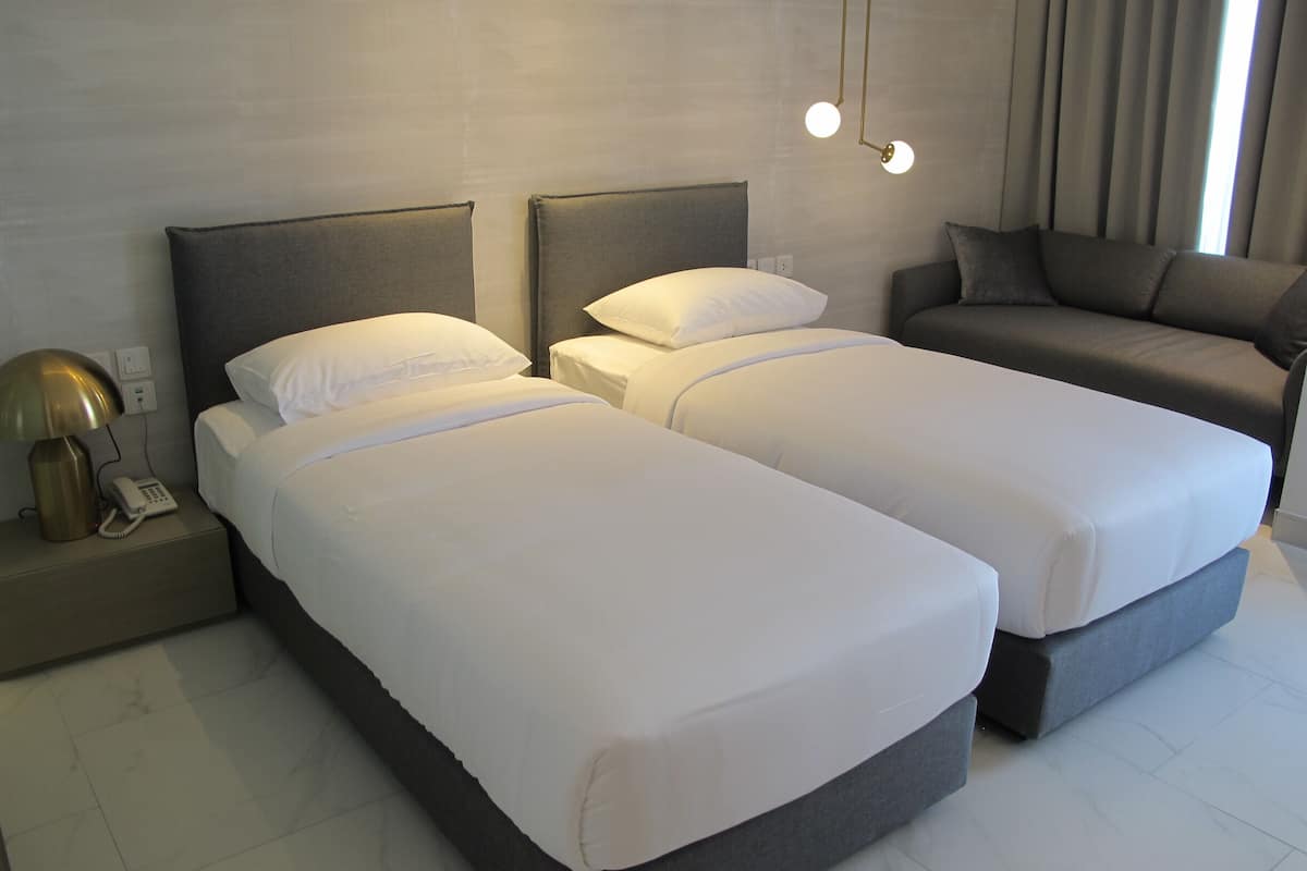 Quarto de hotel com duas camas de solteiro, um sofá, um abajur e um telefone na mesinha de cabeceira.