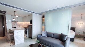 Ein modernes Wohnzimmer mit grauem Sofa, einem Couchtisch und einer Küchenzeile im Hintergrund.