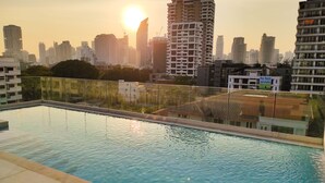 Ein Pool mit Glasgeländer, umgeben von Hochhäusern und einem Sonnenuntergang im Hintergrund.