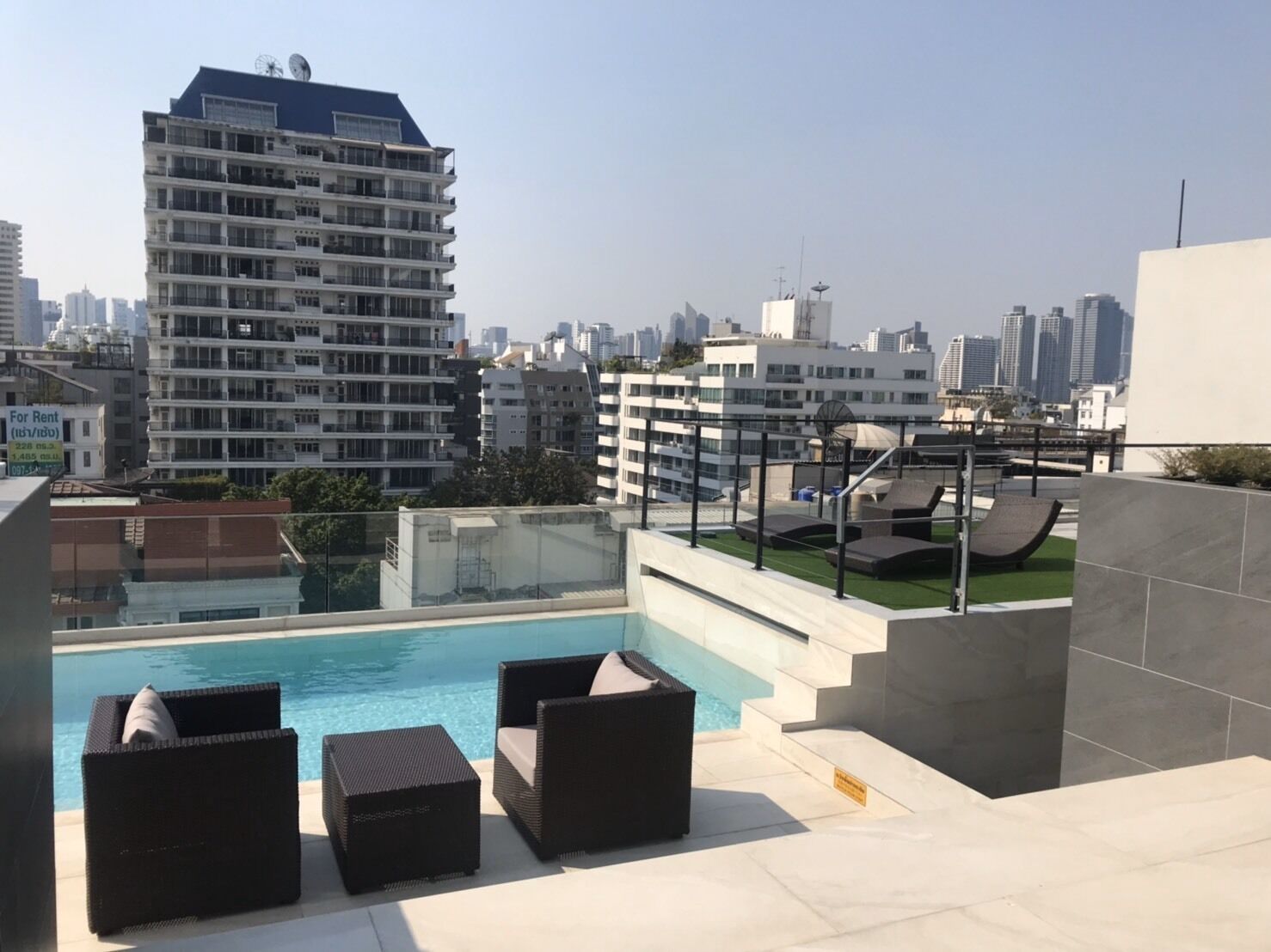 A rooftop pool area with lounge chairs and a view of the city skyline.