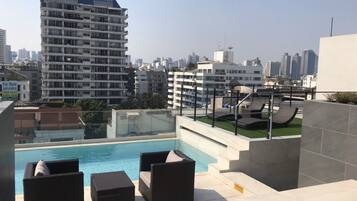 A rooftop pool area with lounge chairs and a view of the city skyline.
