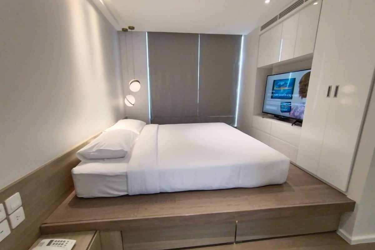 Quarto de hotel moderno com cama, TV integrada e telefone ao lado.