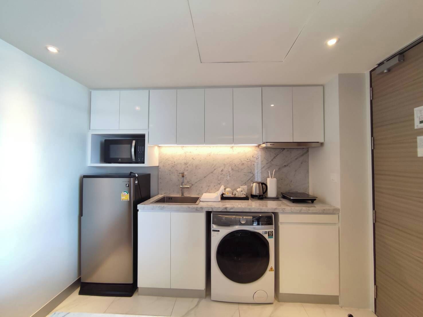 A compact kitchen with a microwave, refrigerator, sink, and washing machine.