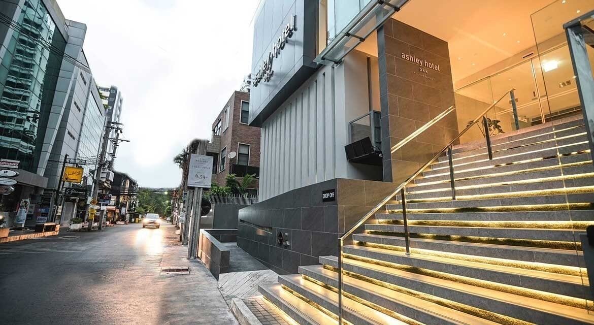 Entrada moderna de hotel con una escalera que lleva al vestíbulo, fachada de vidrio y vista a la calle.