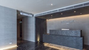 Ein moderner Hotel-Empfangsbereich mit dunklem Marmor-Empfangstresen, einem Hinweisschild zur Orientierung und einem klaren, minimalistischen Design.