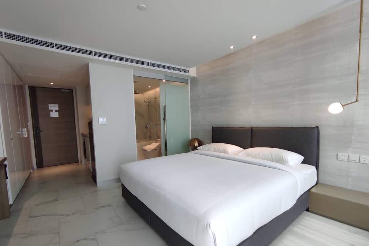 Quarto de hotel moderno com cama grande, closet espaçoso e área de chuveiro.