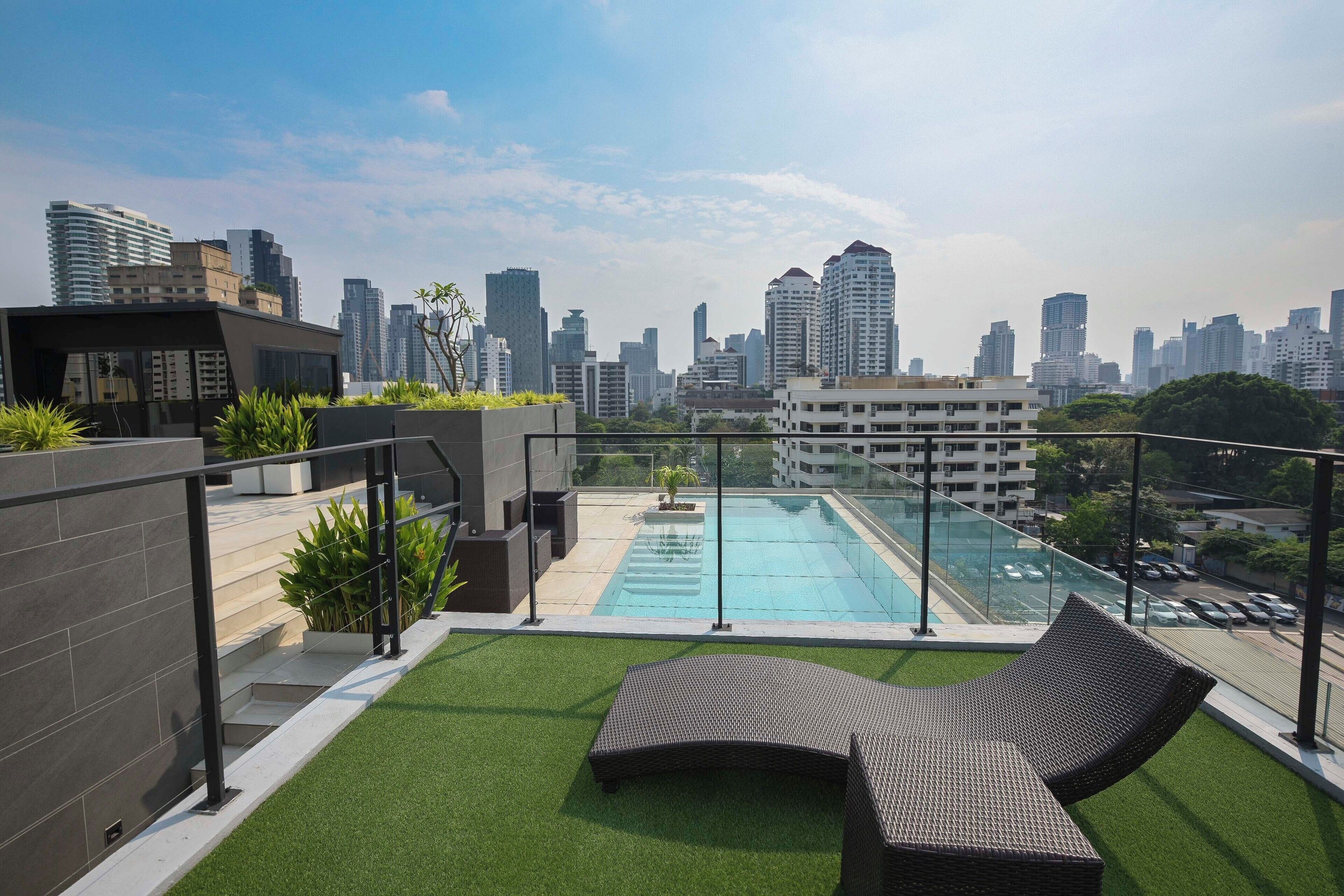 A rooftop pool with a city skyline in the background, surrounded by greenery and modern outdoor furniture.
