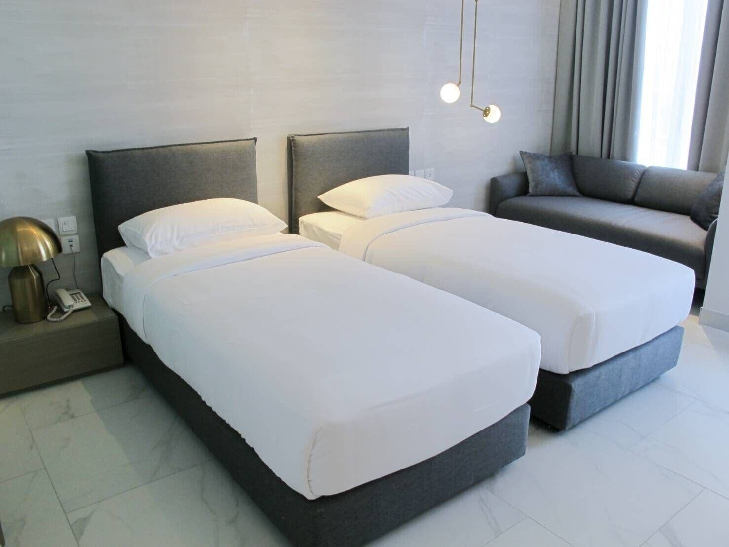 A hotel room with two beds, a sofa, a bedside lamp, and a phone on the nightstand.