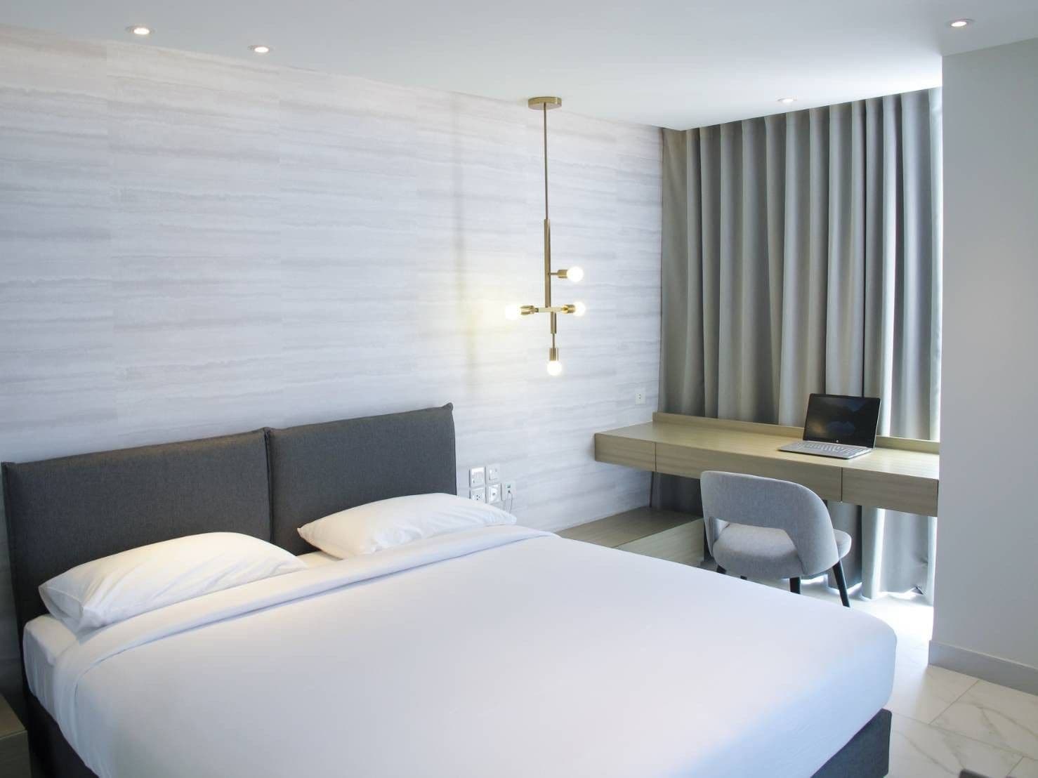 Una habitación de hotel moderna con una cama grande, un escritorio con una computadora portátil y una lámpara colgante.
