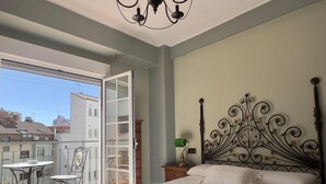 A bedroom with a large bed, a balcony with chairs, and a view of buildings. - Housing León- Marigold (León)
