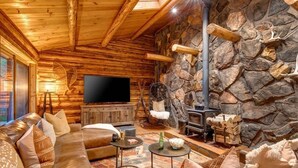 A log cabin interior with a stone wall, wooden furniture, a fireplace, and a television. - Abode at the Aspens, hot tub, near Teton Village (Wilson)